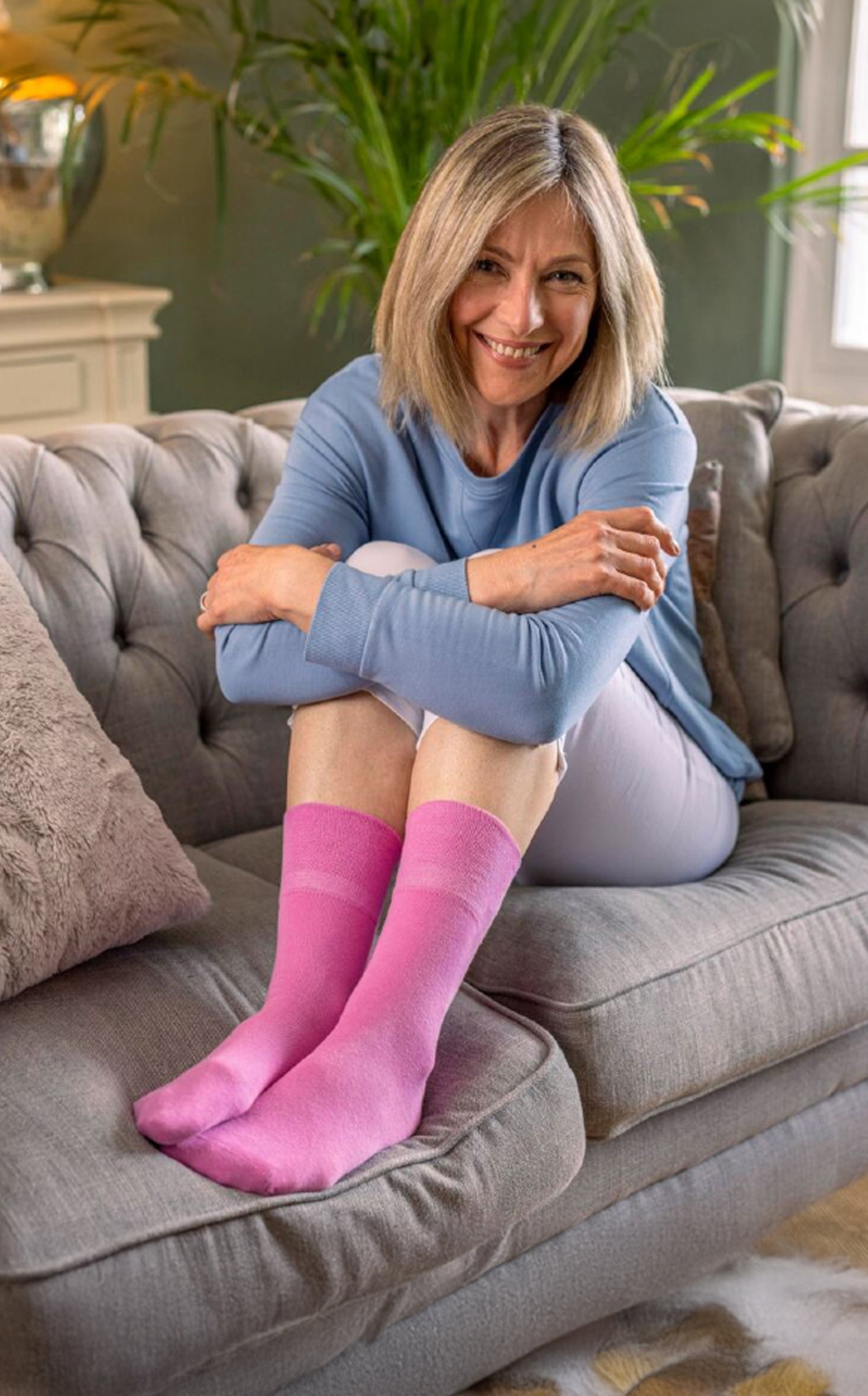 middle aged woman with her knes up and feet on a brown sofa. She is wearing pink soft top socks